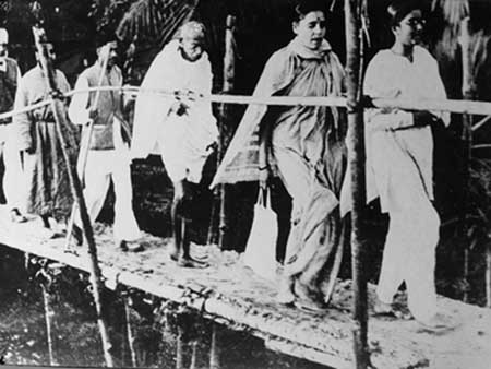 Photograph of Gandhiji while crossing a bamboo poal with Manu Gandhi, Mrs. Sushila Pai, Satyen Chatterjee and Col. Jiwan Singhji.jpg